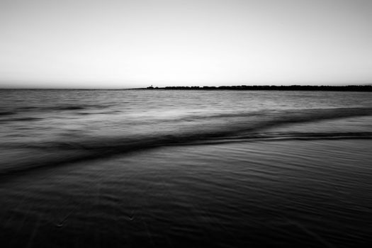 A calming black and white image capturing ocean waves gently reaching the shore at twilight.