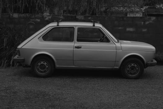 Side view of a classic compact car in black and white, parked outdoors.