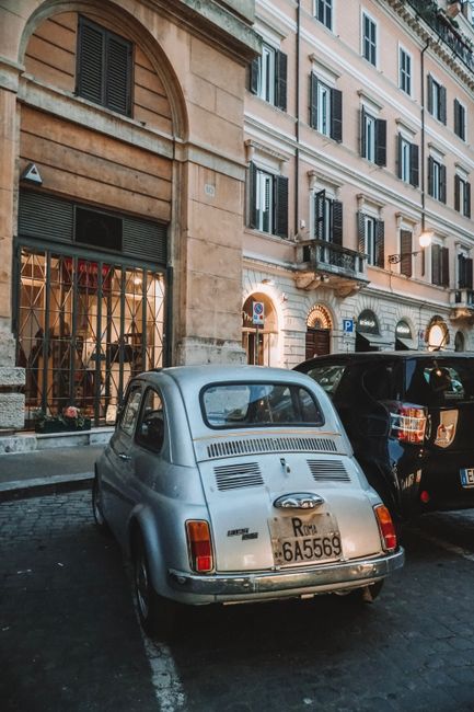 A vintage Fiat 500 parked on a cobblestone street in Rome, Italy, with historic architecture.
