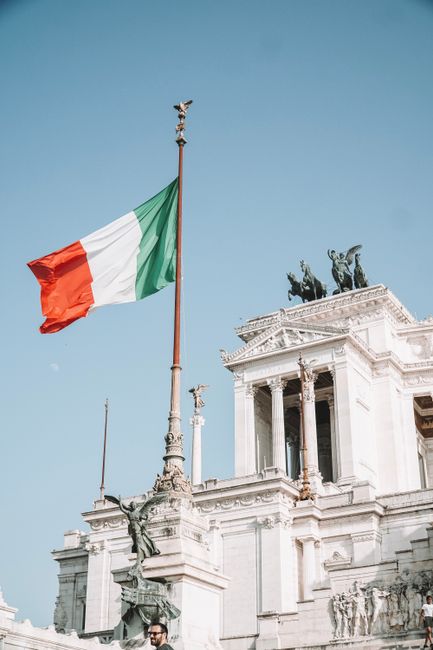Italian flag waving on a monument in Rome with clear sky background, ideal for travel and history themes.
