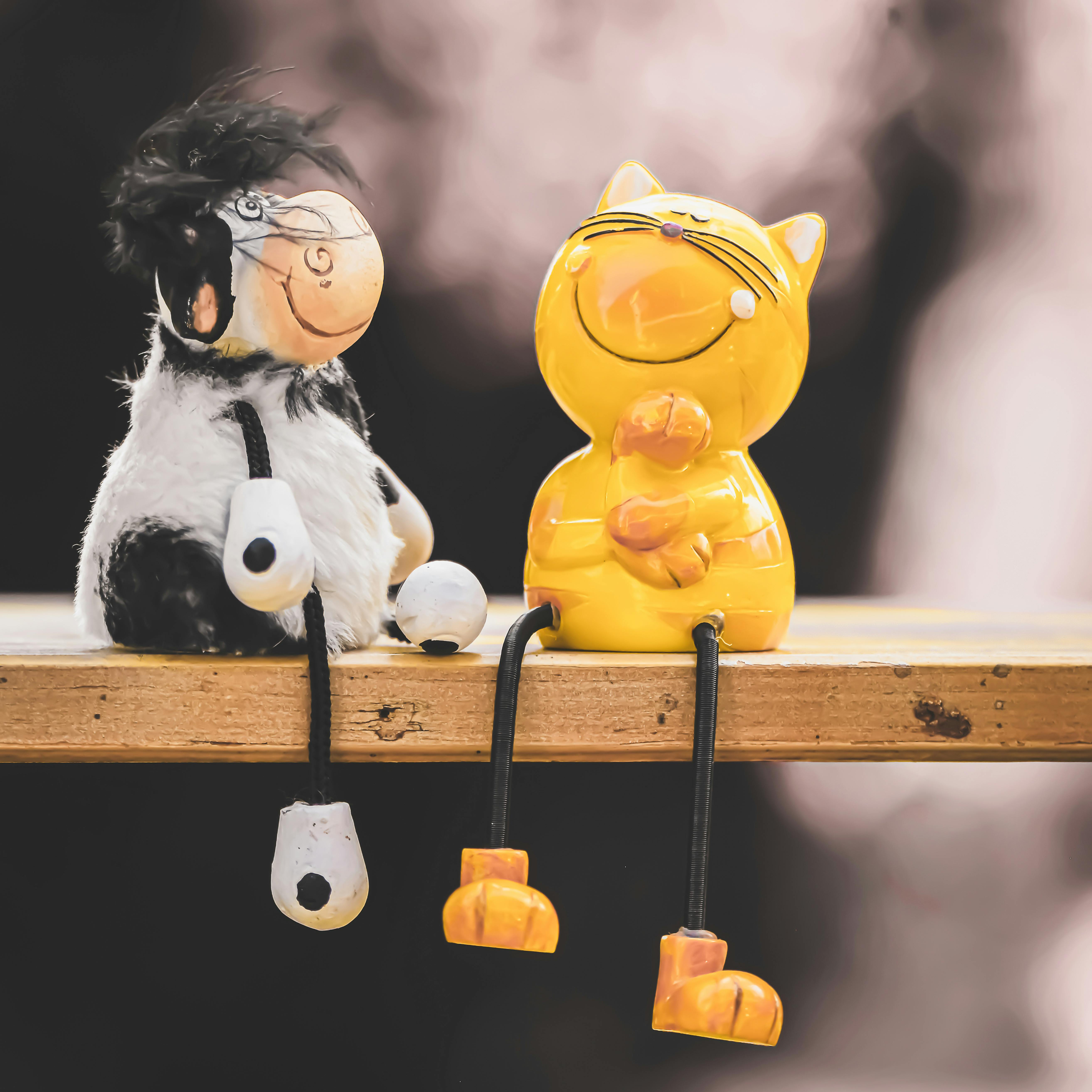 Charming cat and cow figurines sitting on a wooden shelf, captured with selective focus and bright colors.