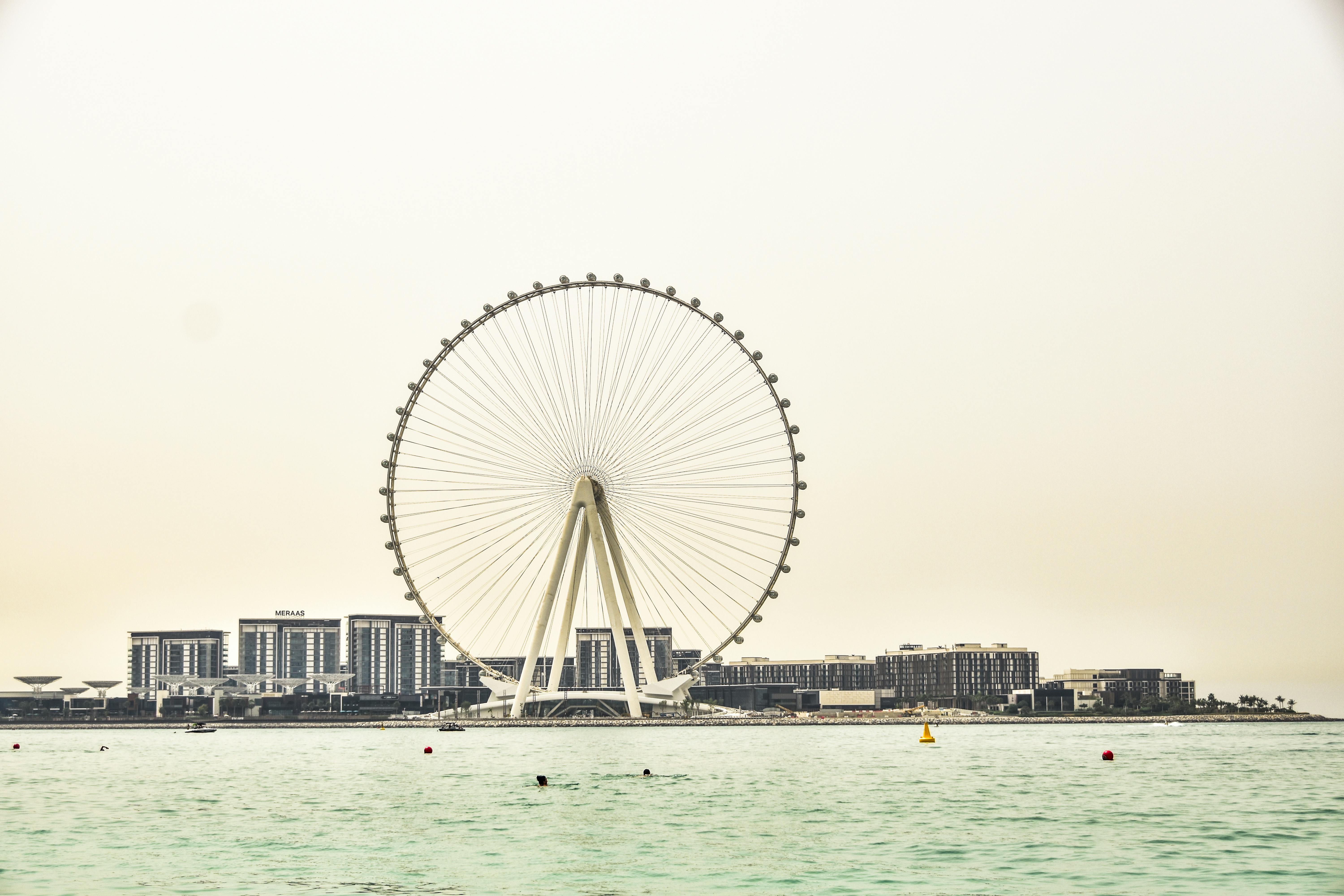 Ferris wheel by waterfront with cityscape backdrop, capturing leisure and urban vibes.