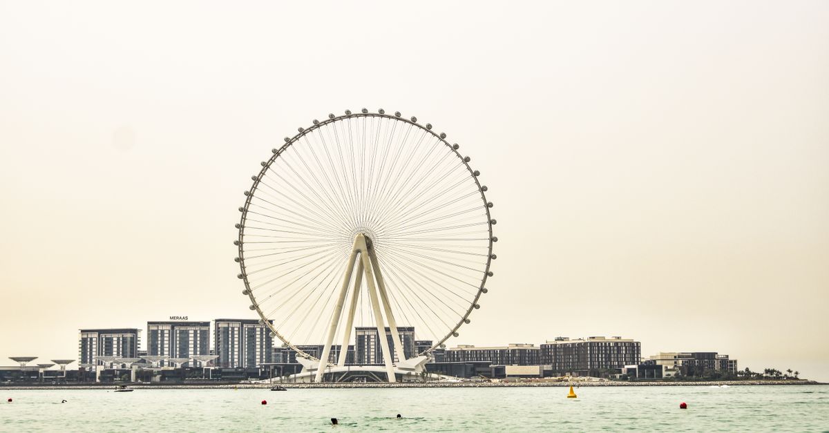 Ferris wheel by waterfront with cityscape backdrop, capturing leisure and urban vibes.