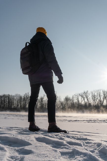 A man stands in a snowy landscape, wearing a backpack, under a clear sky.