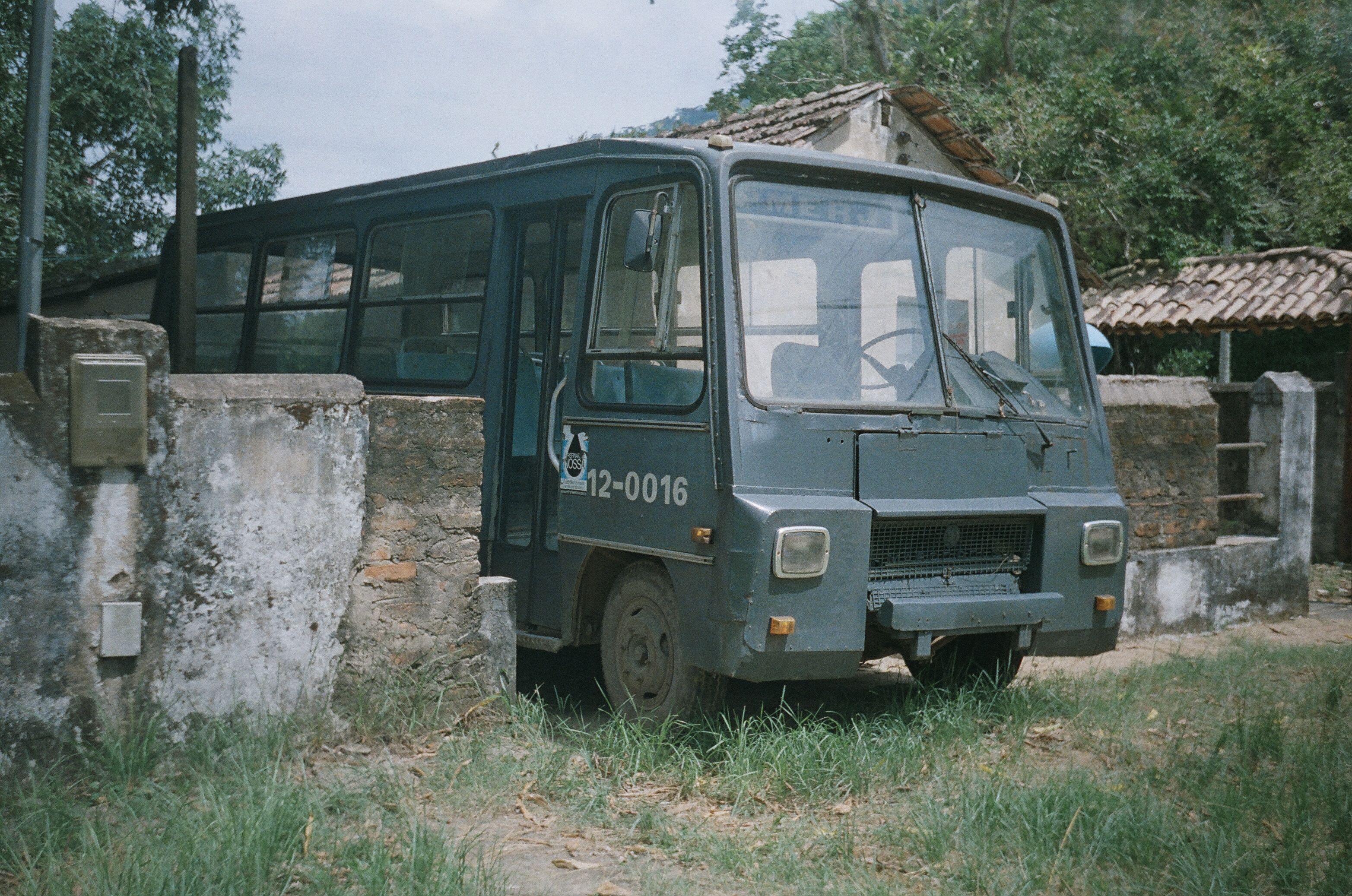 A vintage bus parked near a weathered concrete wall in a rural setting in Rio de Janeiro, Brazil.