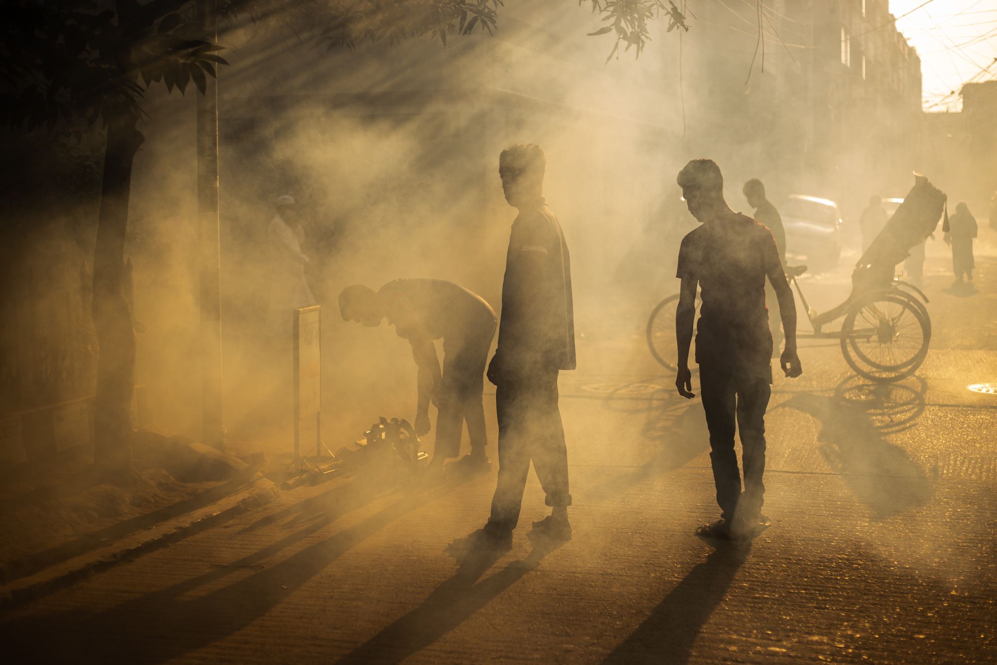 Dramatic scene of people amidst smoke and light on a Dhaka street, creating striking silhouettes.