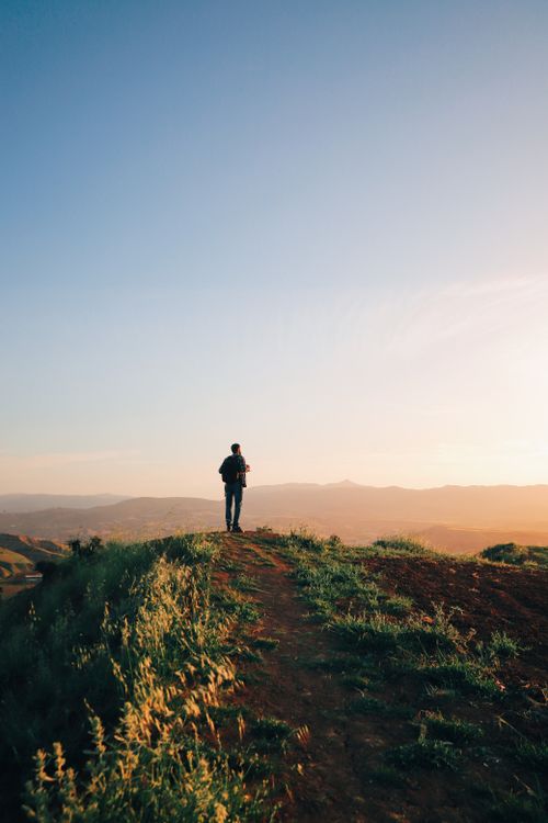 Free Man silhouetted against sunset on hilltop, exploring nature with breathtaking views. Stock Photo