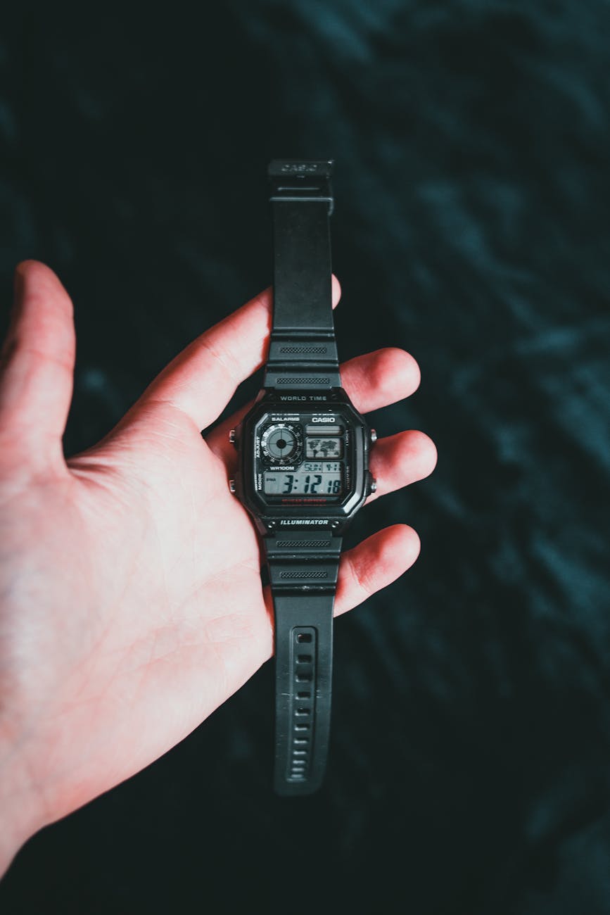 Close-up shot of a hand holding a black digital wristwatch against a dark background.