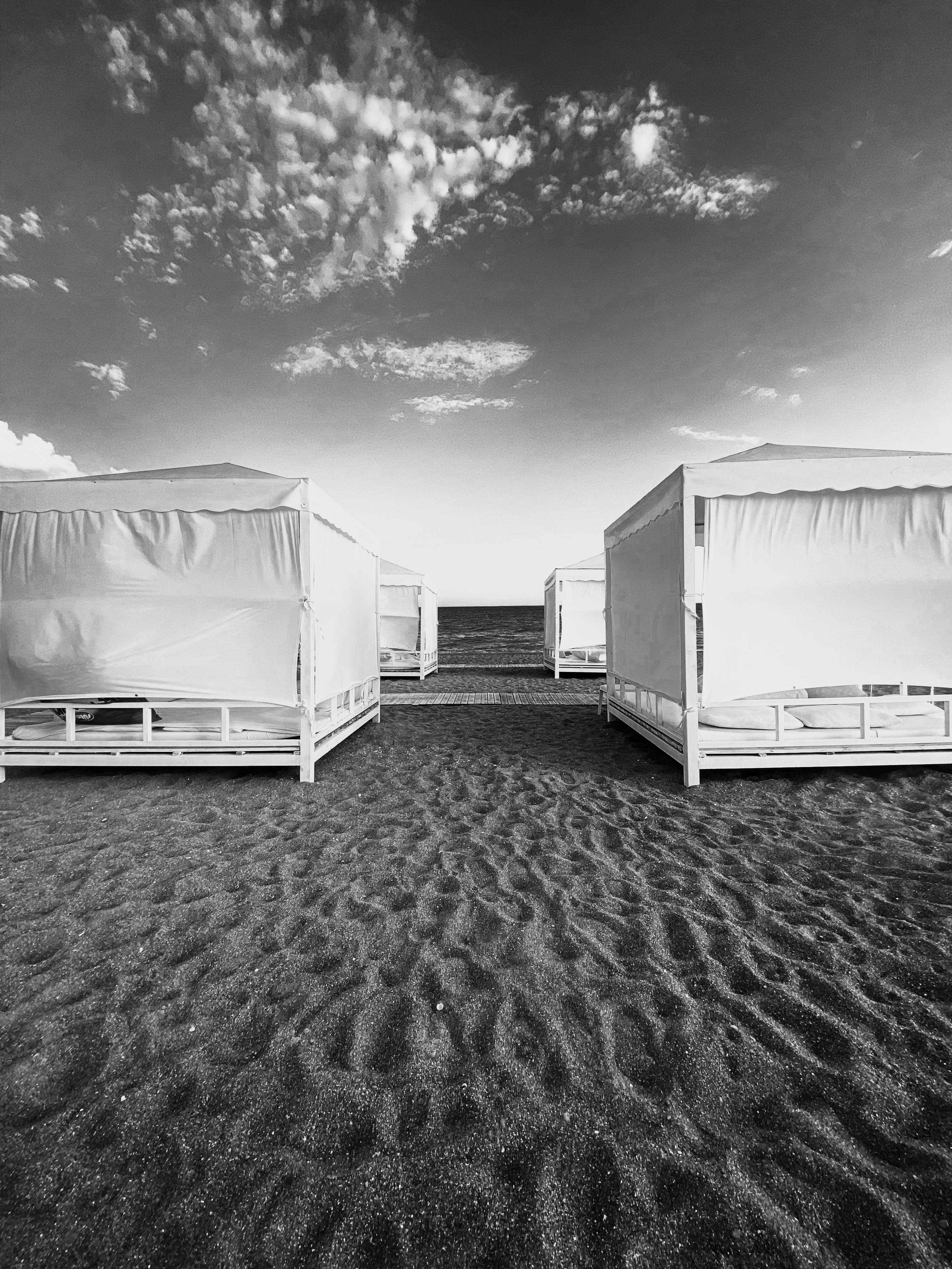 Grayscale image of beach cabanas lined up on a sandy shore, offering a serene coastal view.