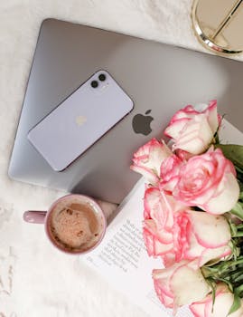 Elegant flat lay of a laptop, iPhone 11, pink roses, and coffee on a fluffy surface.