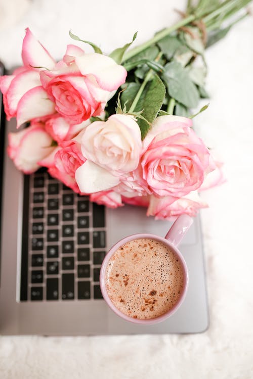 Close-Up Shot of a Coffee and Bouquet of Roses on Top of a Laptop