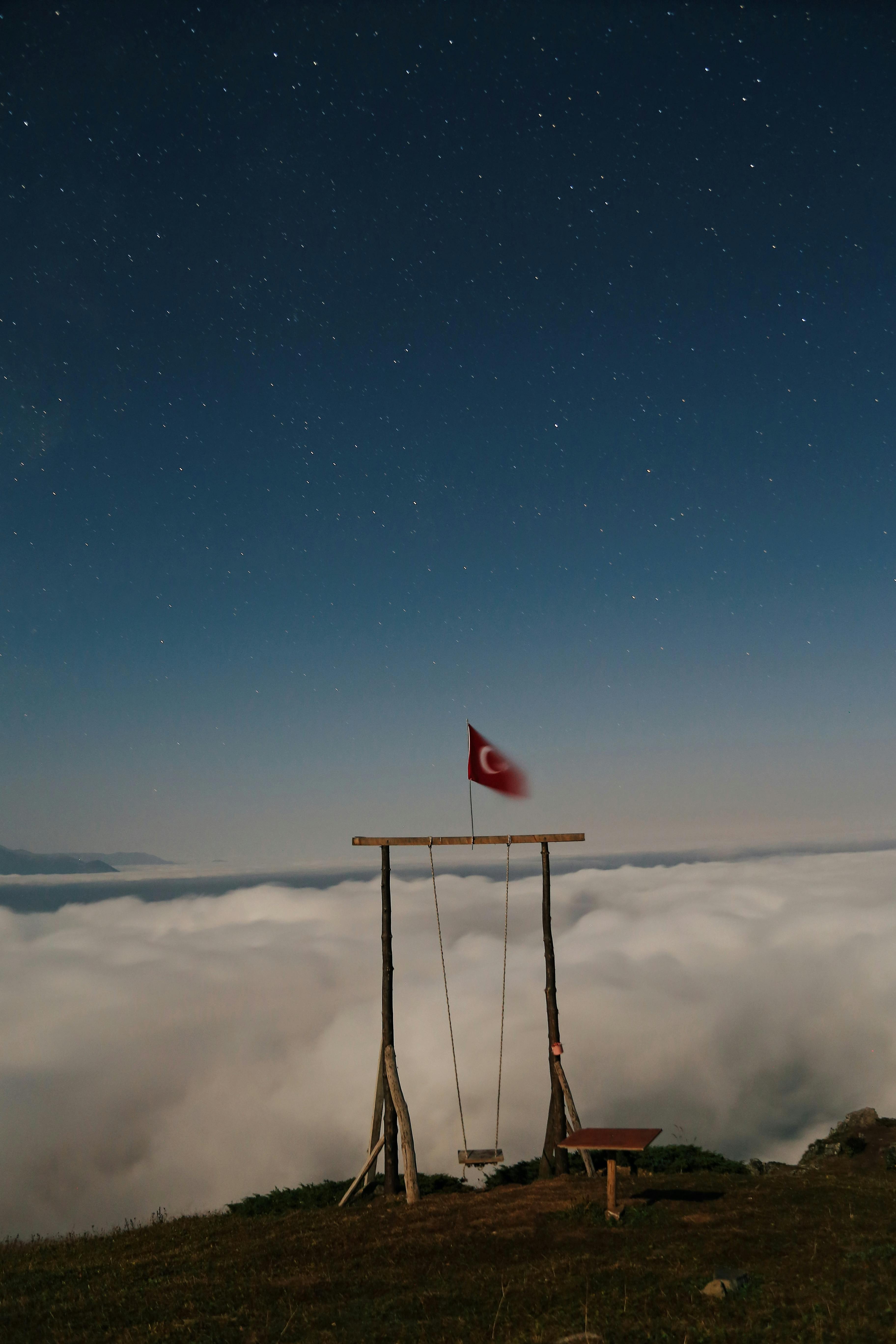 A swing with a Turkish flag, above clouds, under a starry night sky.