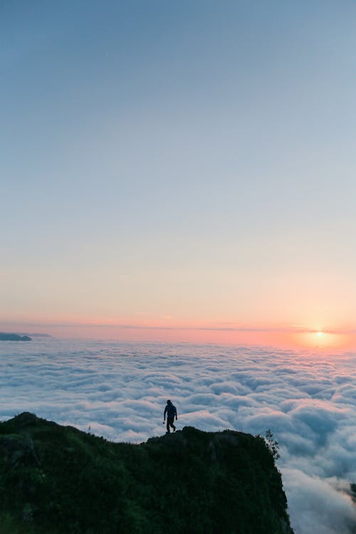 Person Standing on Rock Formation Overlooking White Clouds