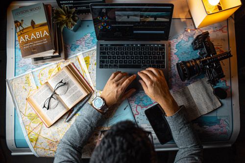 Free Man planning travel itinerary using laptop and maps at desk. Stock Photo