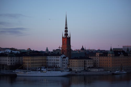 Riddarholmen Church and aged house exteriors against motor ship on water under cloudy sky at sunset in Stockholm Sweden
