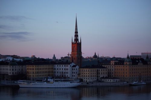 Free Riddarholmen Church and aged house exteriors against motor ship on water under cloudy sky at sunset in Stockholm Sweden Stock Photo
