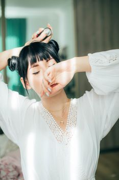 Young woman stretching indoors with perfume bottle, embracing morning relaxation.