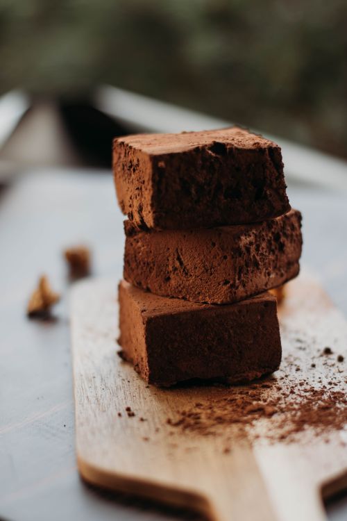 Free Three stacked chocolate brownies with cocoa powder on a wooden board. Perfect for dessert imagery. Stock Photo