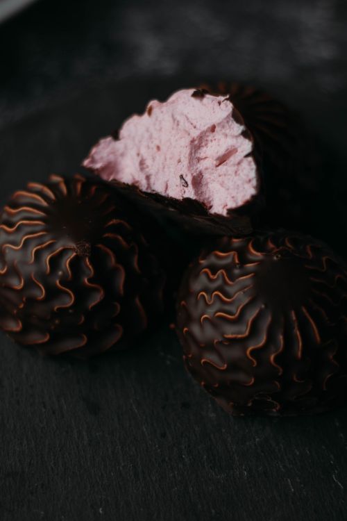 Free Delicious chocolate-coated pastries filled with vibrant pink cream on dark surface. Stock Photo