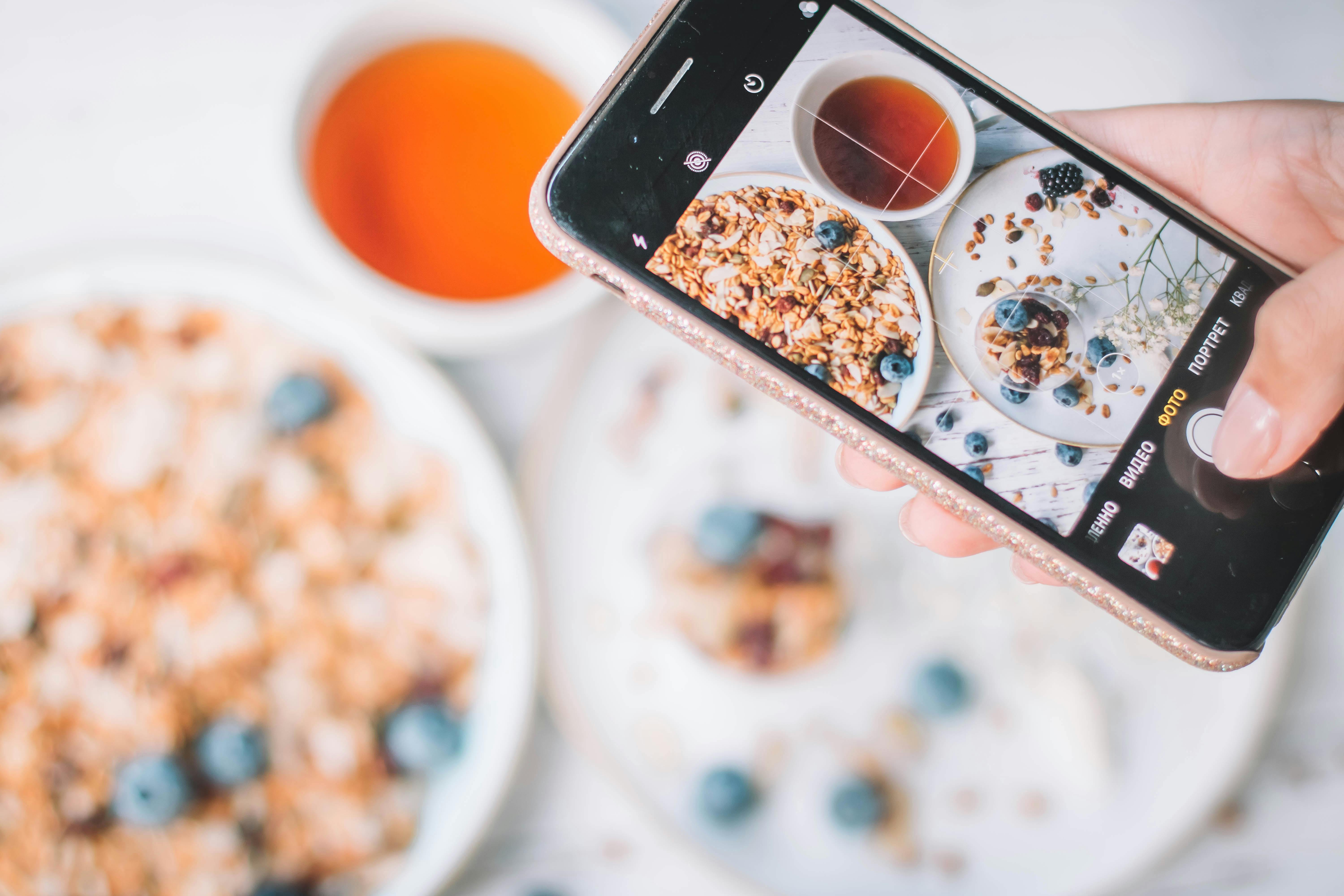 Free A smartphone capturing a healthy breakfast bowl with blueberries and tea. Stock Photo