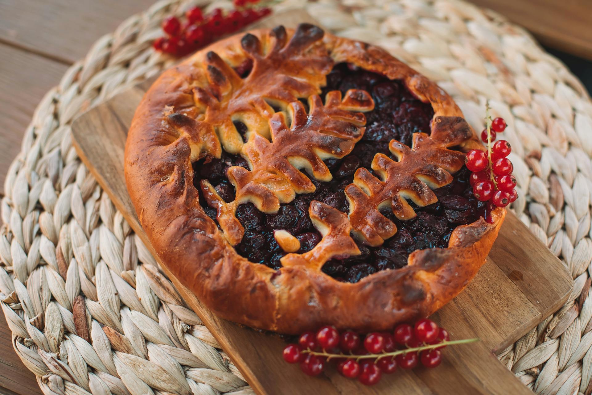 Delicious homemade berry pie with decorative crust on wooden board and woven mat.