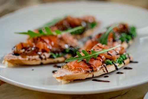 Free Close-up of gourmet salmon bruschetta with fresh arugula on a ceramic plate. Stock Photo