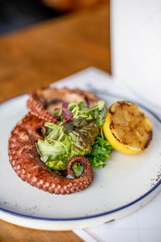 High angle of savory fried octopus tentacles served with lettuce leaves and lemon on plate