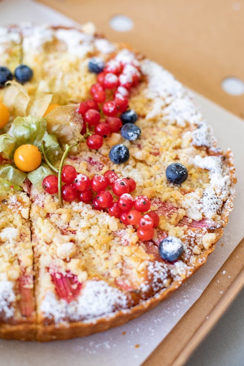 High angle of palatable sweet crumble pie with various berries placed on paper and cardboard