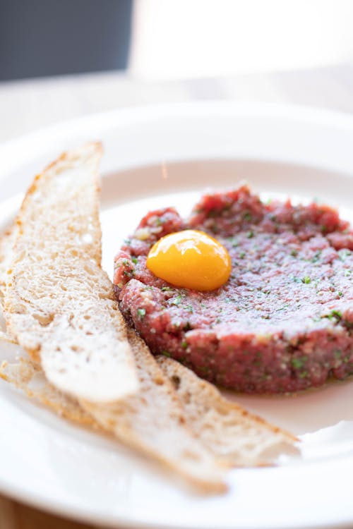 Savory beef tartare dish with raw egg yolk served on plate near crunchy croutons during lunch