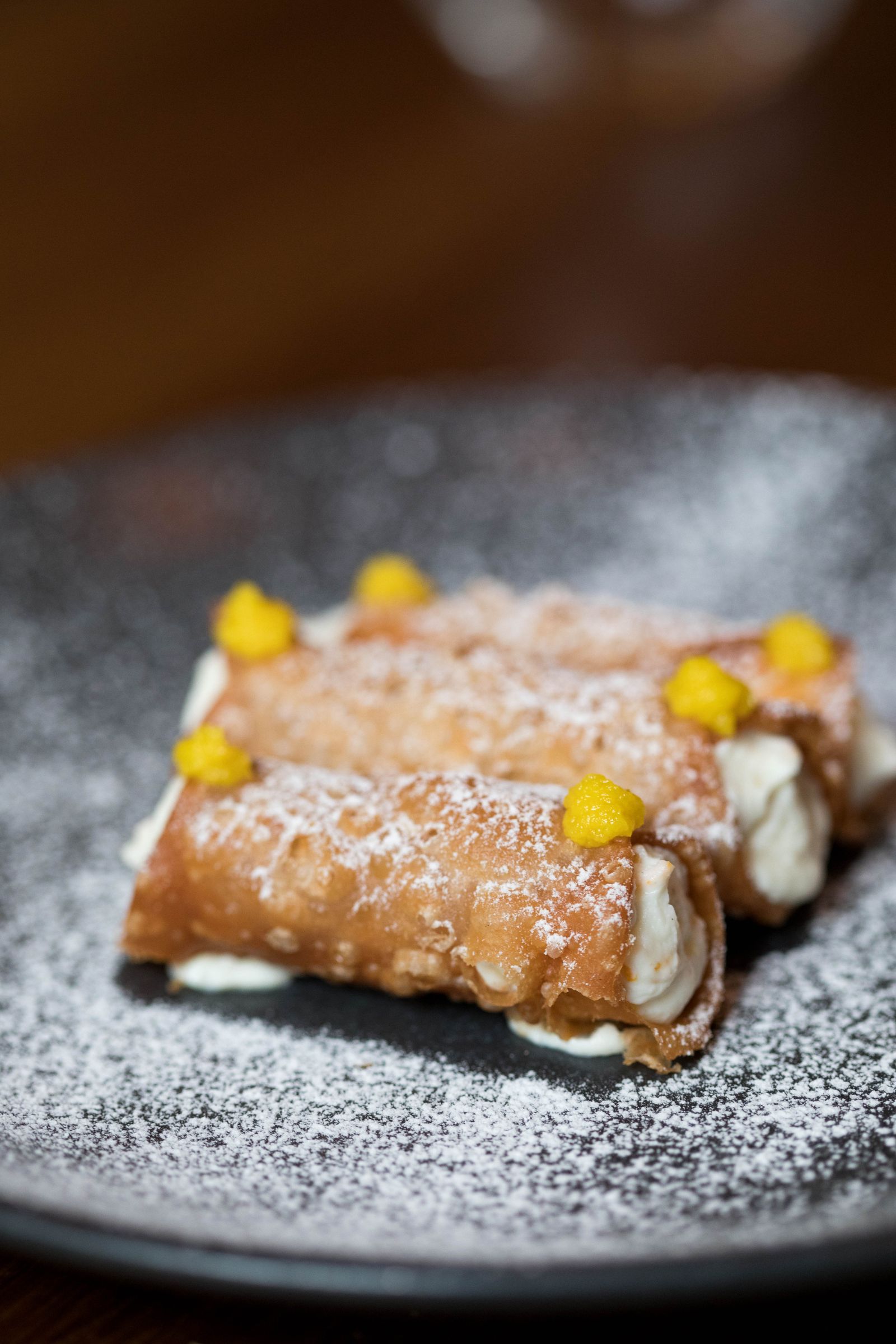 Cannoli with cream filling and powdered sugar on a dark plate