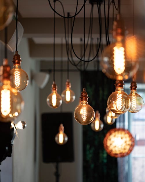 Bunch of vintage electric light bulbs hanging on wires and glowing inside cozy cafe