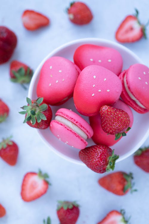 Top view of ceramic plate with vivid fruit macaroons and ripe strawberries placed on gray table