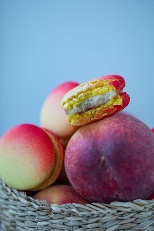 Tasty macaroons and fresh peaches placed in wicker basket on blue background