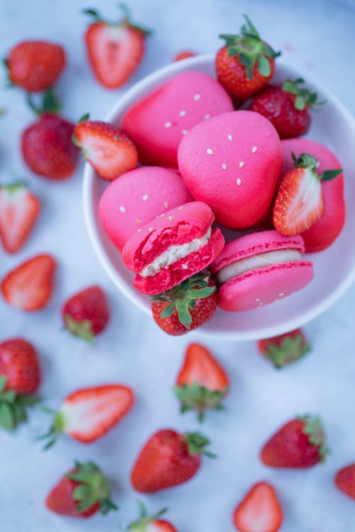 From above fresh macaroons placed on plate on gray table with ripe strawberries