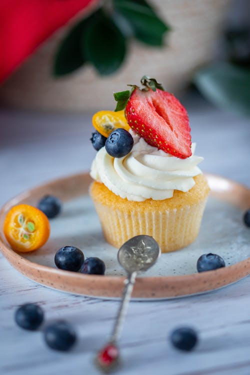 Free Cupcake with cream decorated with fresh strawberry and blueberries with spoon on blurred background Stock Photo