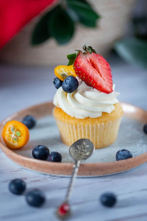 Free Cupcake with cream decorated with fresh strawberry and blueberries with spoon on blurred background Stock Photo