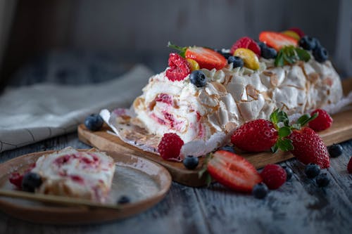 Tasty sweet meringue roll garnished with fresh berry mix and tender cream served on wooden board and plate