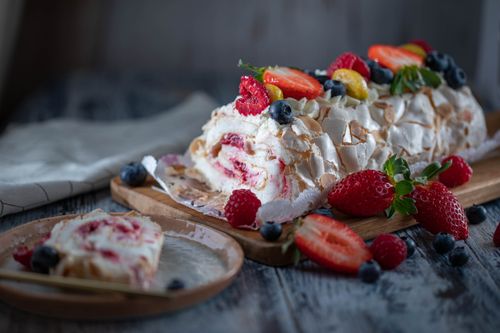 Free Tasty sweet meringue roll garnished with fresh berry mix and tender cream served on wooden board and plate Stock Photo