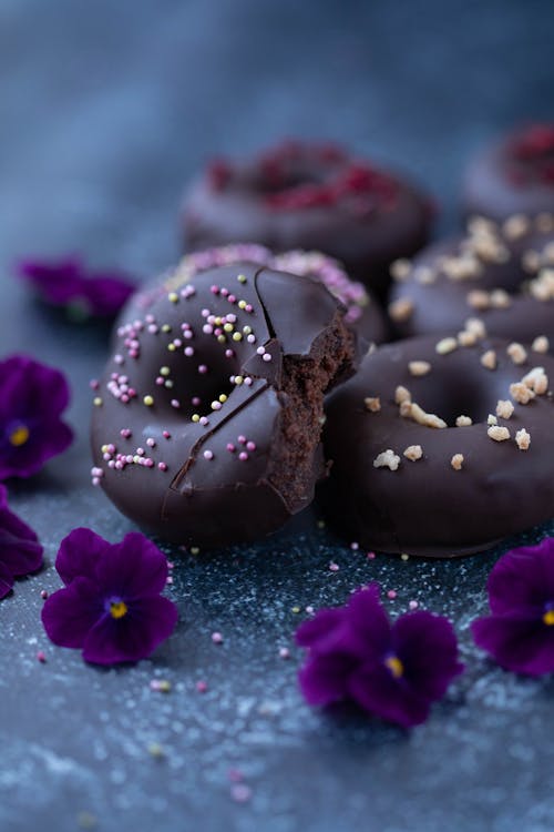 Tasty sweet chocolate donuts with sprinkles near violet blooming flowers