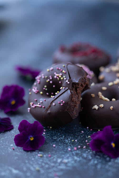 High angle of tasty donuts with chocolate glaze and sprinkles placed plate decorated with small aromatic Viola flowers