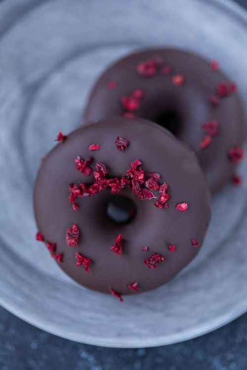 Free From above of tasty chocolate coated donuts with red freeze dried berry sprinkles placed on gray plate in daytime Stock Photo