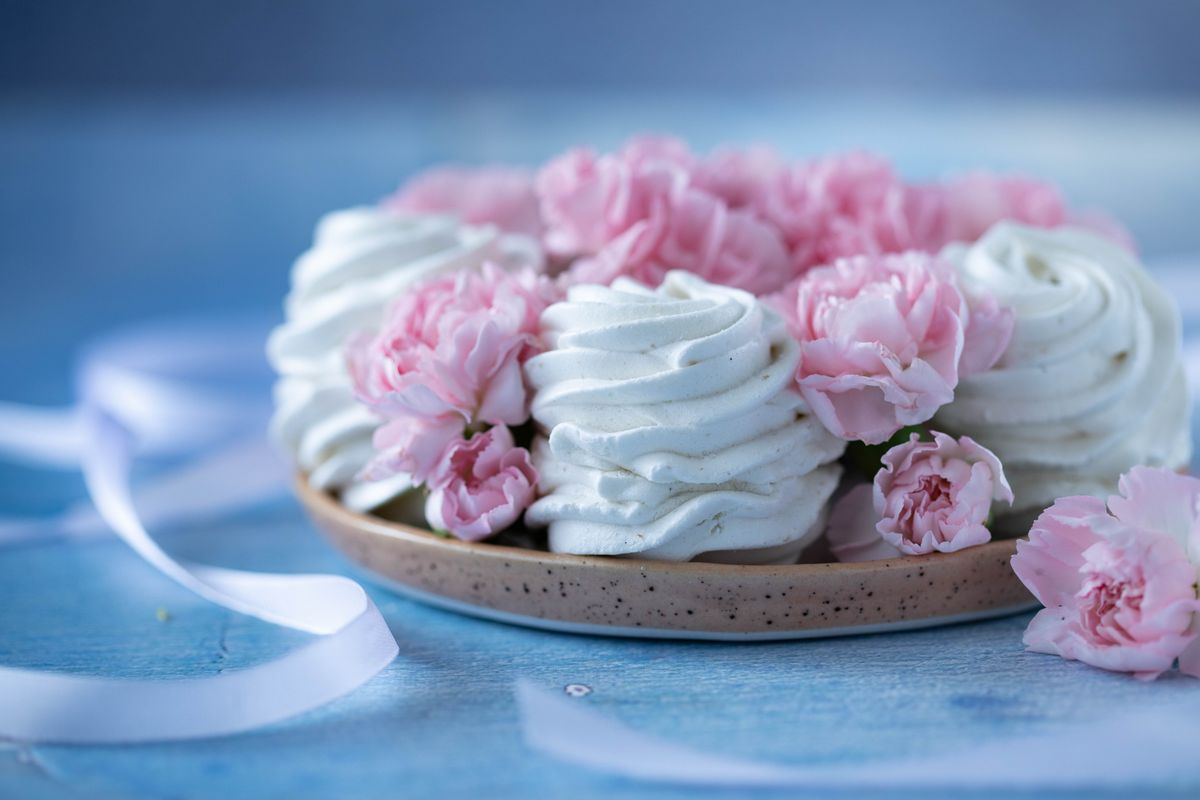 Delicious sweet marshmallows placed on plate decorated with small pink flowers on blue table against blurred background