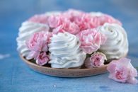 From above of delicious white marshmallows zephyr and buds of pink flowers placed on plate on blue table in room against blurred background