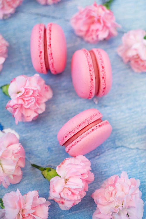 Free From above of tasty pink macaroons and aromatic carnations placed on blue table in daytime Stock Photo
