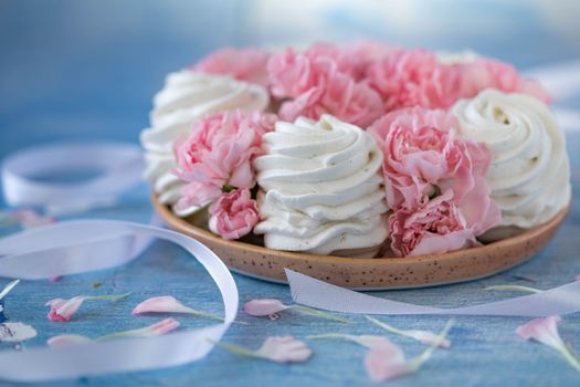 White zephyrs near pink peonies on ceramic plate near ribbons and petals on blue tablecloth in light room