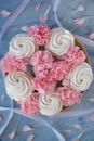 Top view of sweet white zephyr decorated with pink flowers placed on table with petals and ribbons in light room