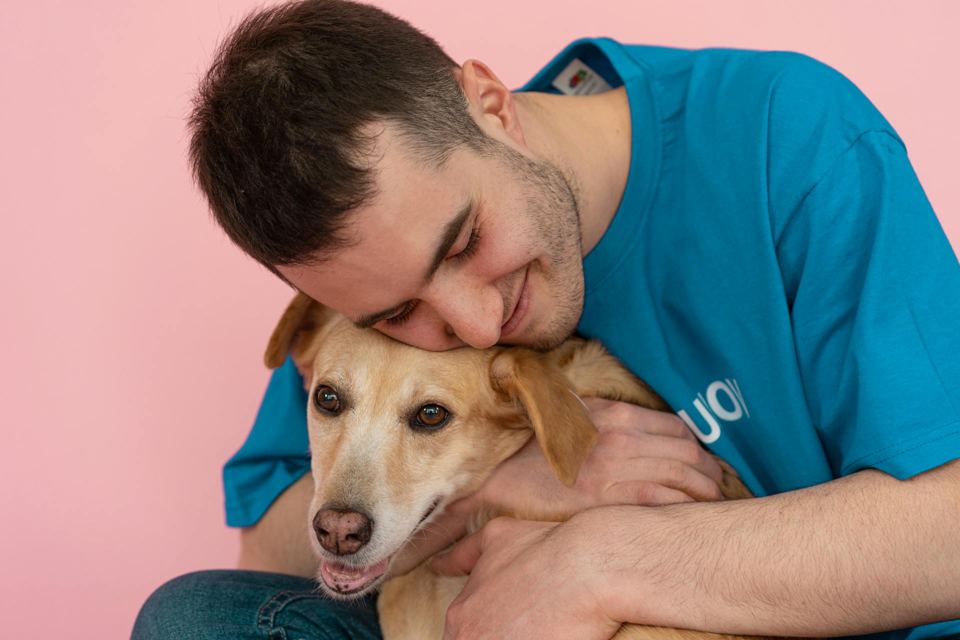 A Man in Blue Crew Neck T-shirt Embracing a Brown Dog