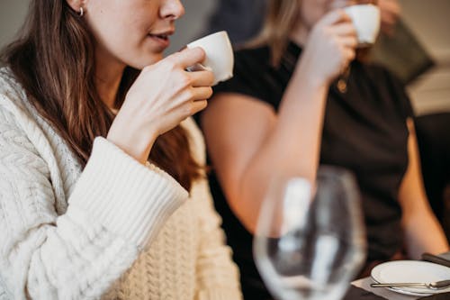 Free Crop unrecognizable female drinking hot espresso from small white cups while sitting at table with dishware in modern light cafe Stock Photo