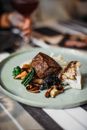 Tasty steak served on plate with white cauliflower and fried mushrooms placed on table in light modern restaurant on blurred background