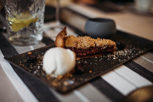 Slice of tasty crumble pie with berry filling on plate with scoop of ice cream served on table in restaurant on blurred background